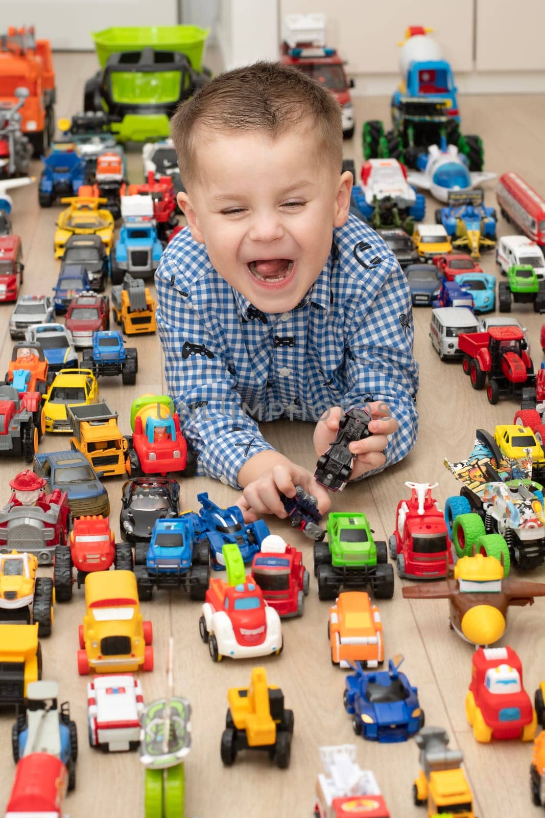 Concept of children's toys. A little boy, 4 years old, plays happily, lying on the floor, with colorful small and large cars in the children's room. Soft focus.