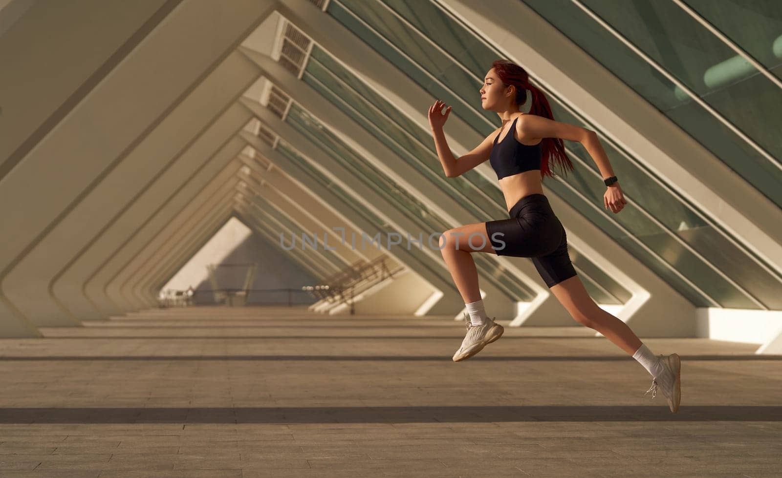 Active woman athlete is jogging on morning on modern building background. Healthy life concept by Yaroslav_astakhov