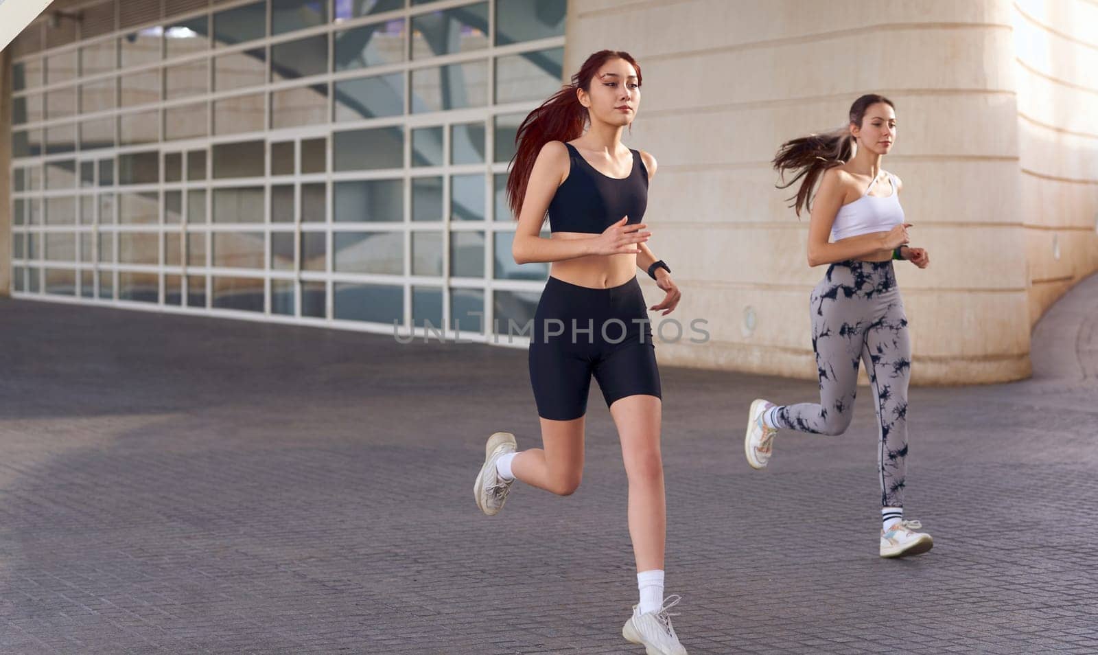 Active women athlete running on sunny morning side by side on modern building background by Yaroslav_astakhov