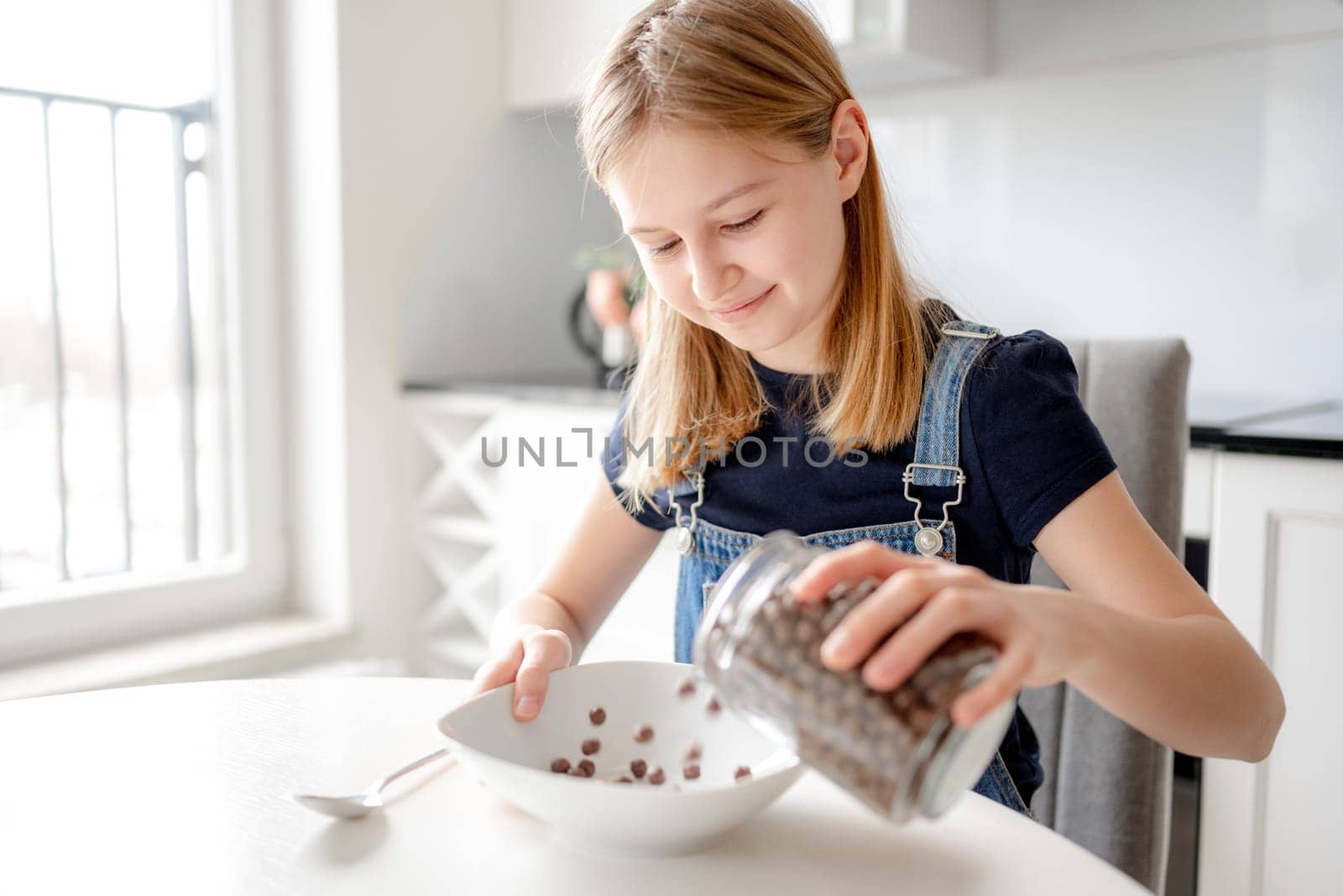 Sweet Girl Pours Flakes Into Plate For Dry Breakfast In Kitchen