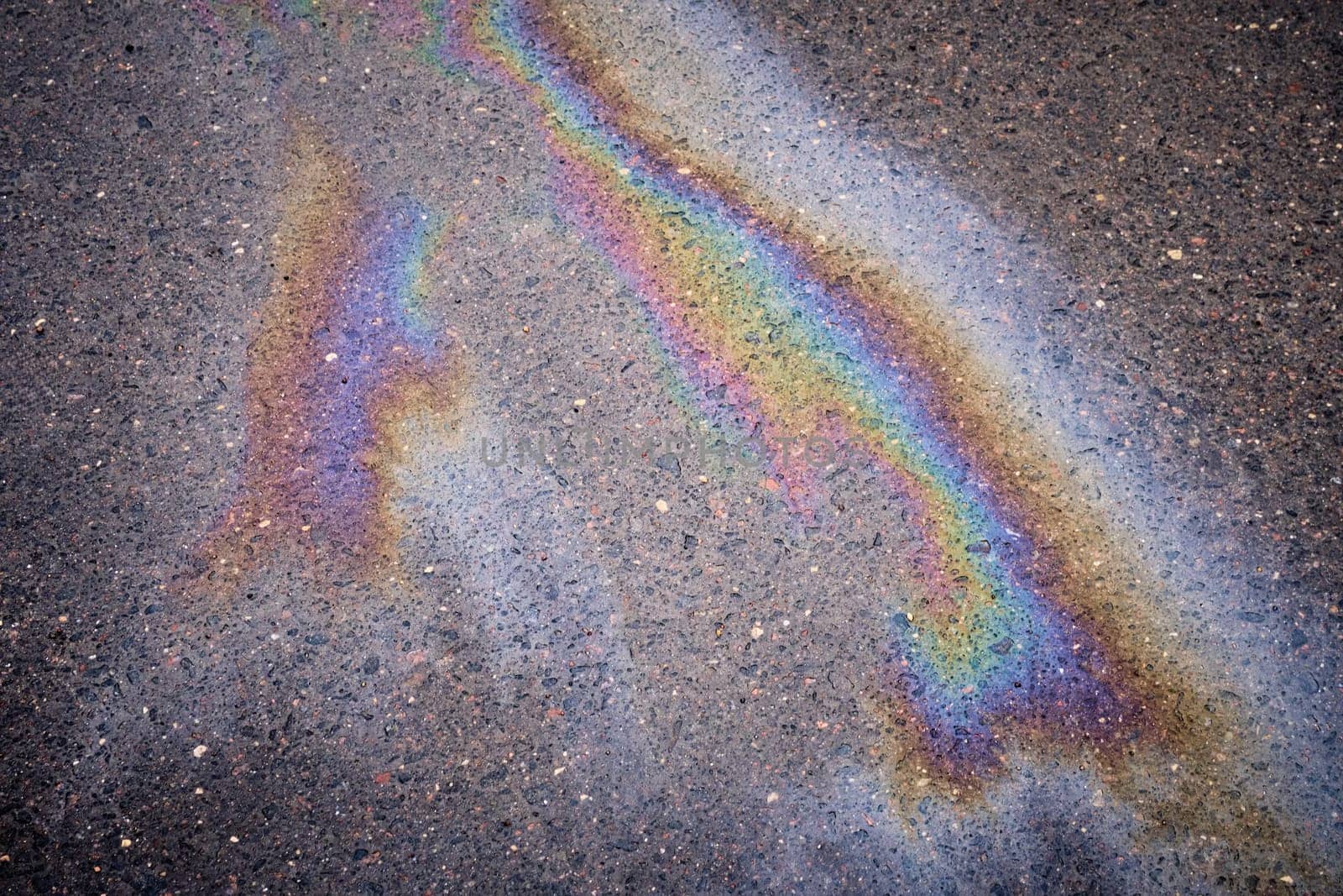 An oil slick on wet asphalt surface. Picture of oil or gasoline spill on asphalt.