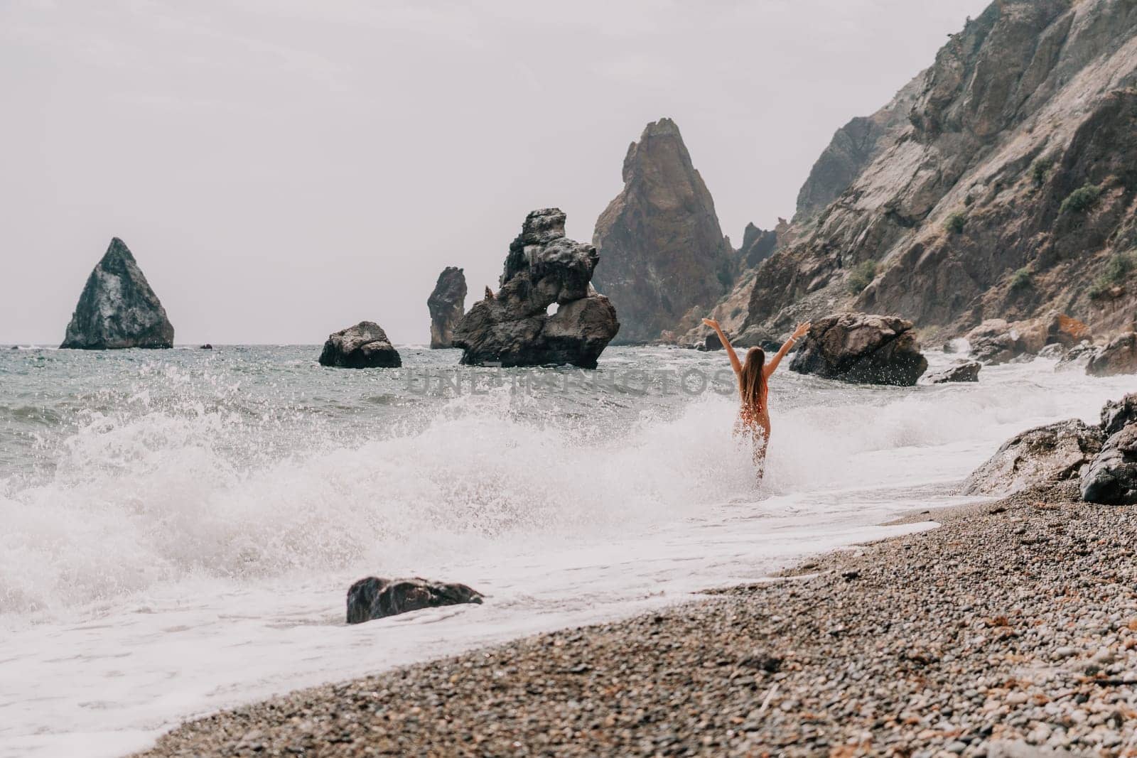 Woman travel sea. Young Happy woman in a long red dress posing on a beach near the sea on background of volcanic rocks, like in Iceland, sharing travel adventure journey