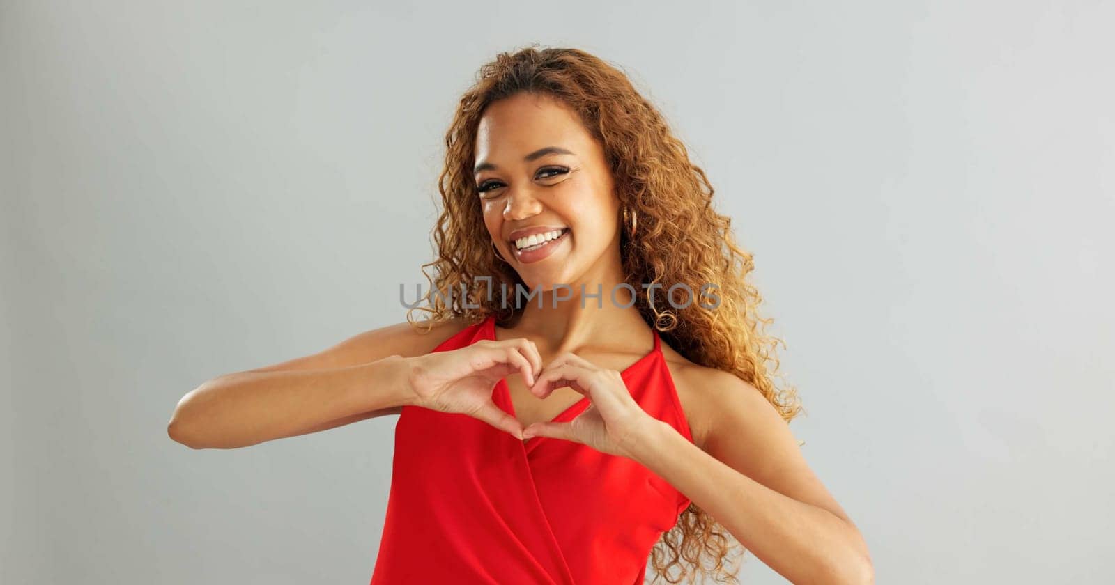 Happy woman, love and support with heart hands for romance or care on a gray studio background. Portrait of female person or model with smile, like emoji or shape for valentines day on mockup space.