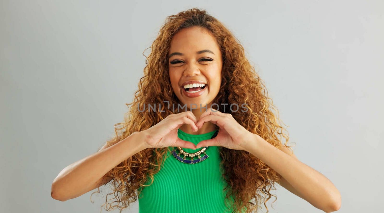 Happy woman, love and care with heart hands for romance or trust on a gray studio background. Portrait of female person or model with smile, like emoji or shape for romantic gesture on mockup space.