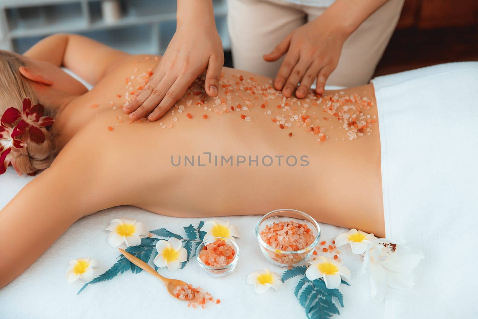 Woman customer having exfoliation treatment in luxury spa salon with warmth candle light ambient. Salt scrub beauty treatment in health spa body scrub. Quiescent