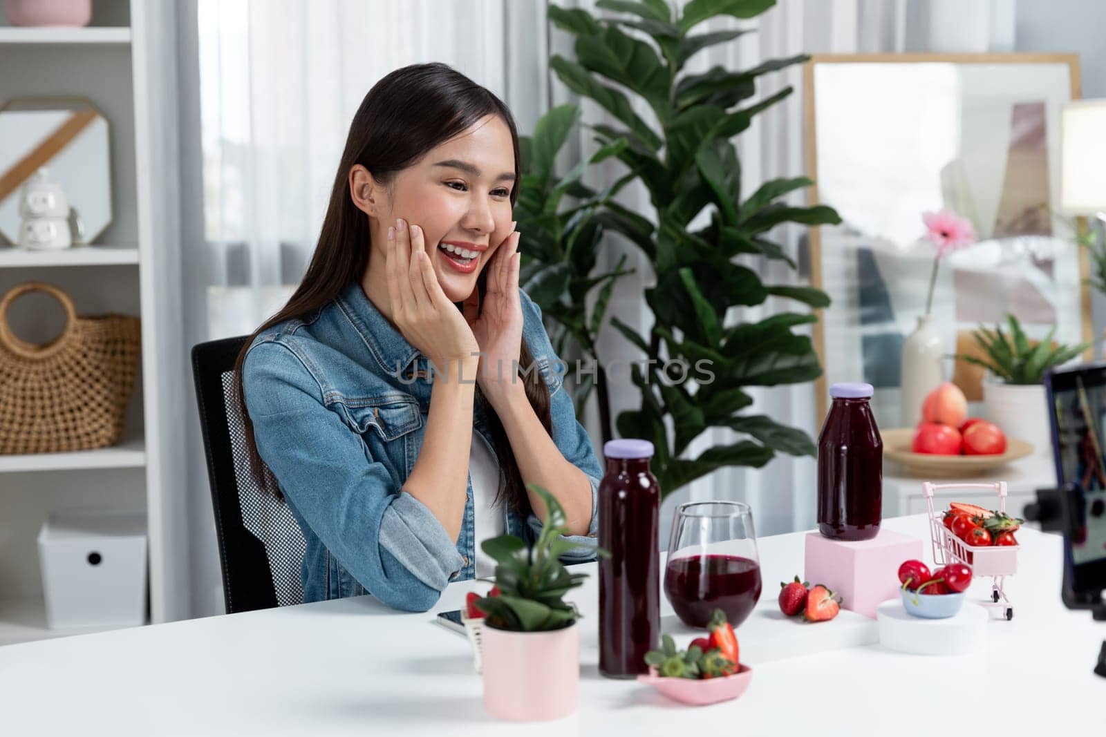 Smiling young beautiful Asian reviewing tasty mixed strawberry and cherry juice detox drinks, showing healthy product to promote for special promotion selling on social media online record. Stratagem.