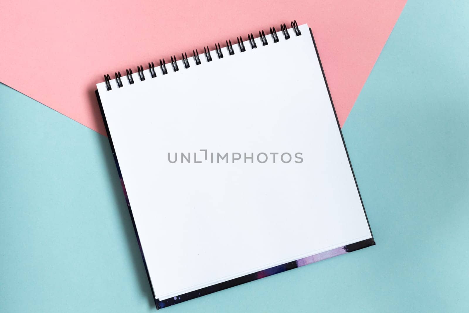 Top view of open notebook with clean sheet. Template for message. Empty spiral sketchbook with white paper on pastel pink and blue background