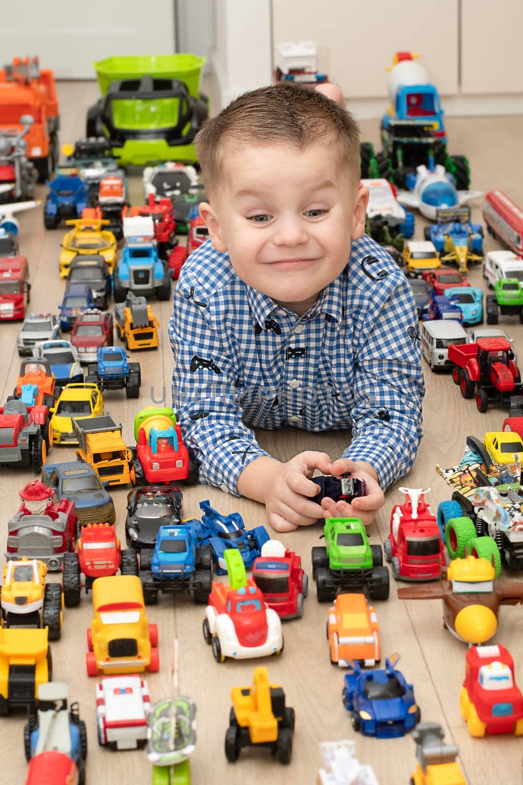 Concept of children's toys. A little boy, 4 years old, plays happily, lying on the floor, with colorful small and large cars in the children's room. Soft focus.