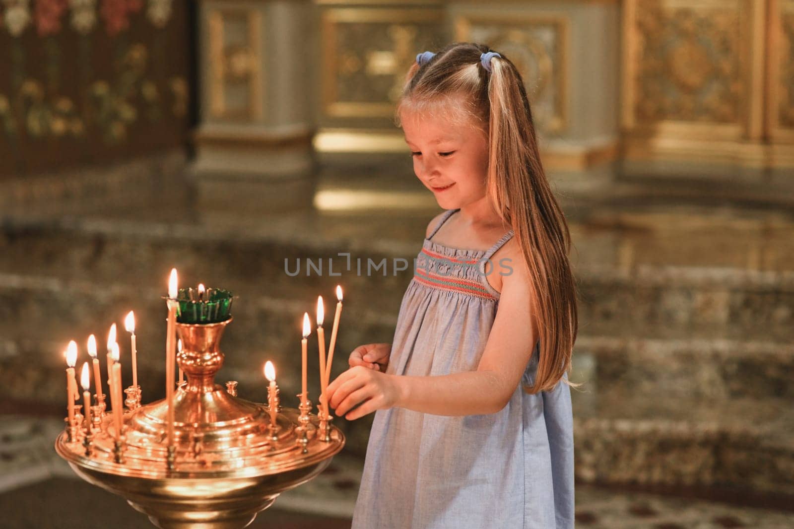 A little girl puts a candle in church. Orthodoxy by Godi