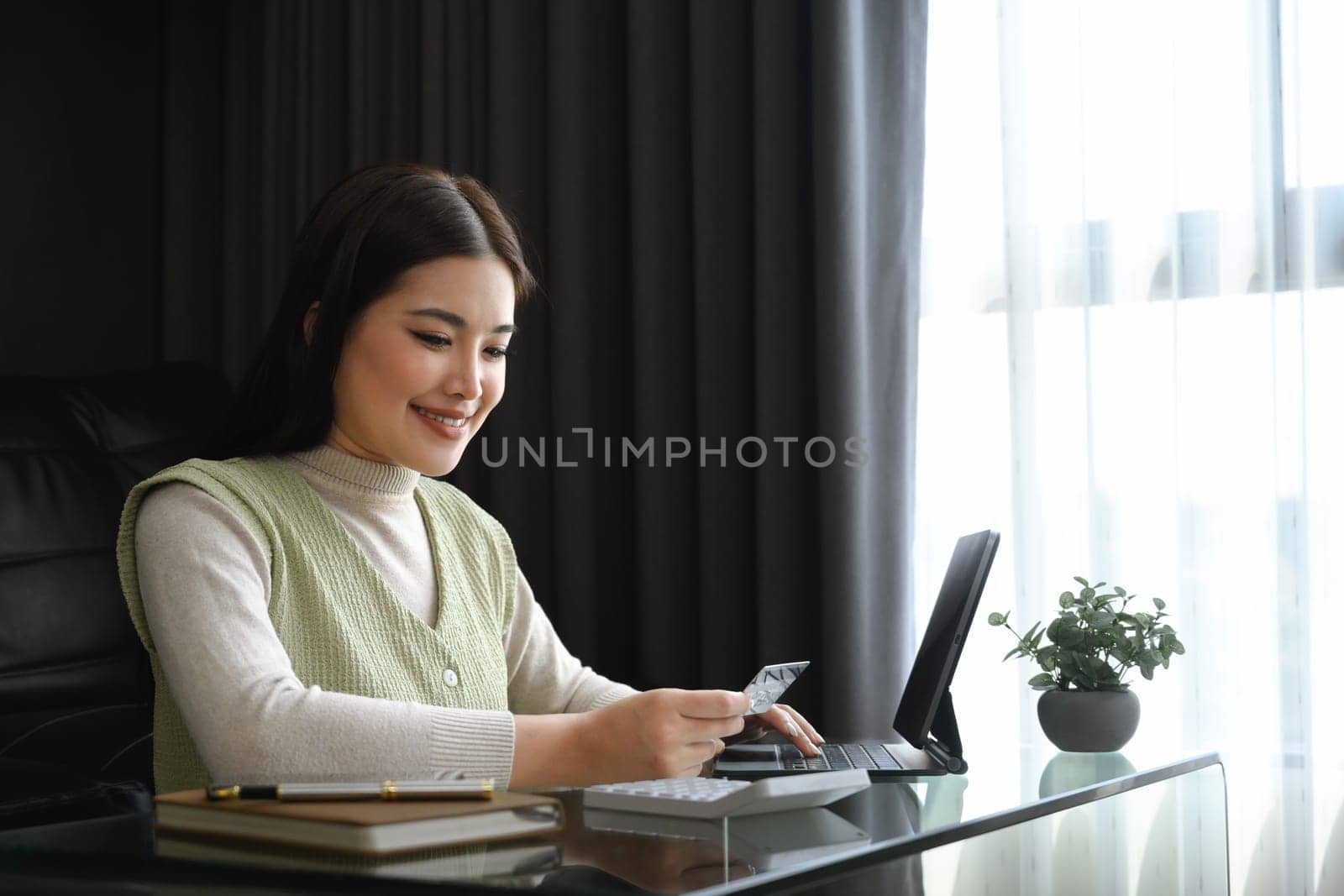 Attractive young woman holding credit card and calculating monthly expenses at home.