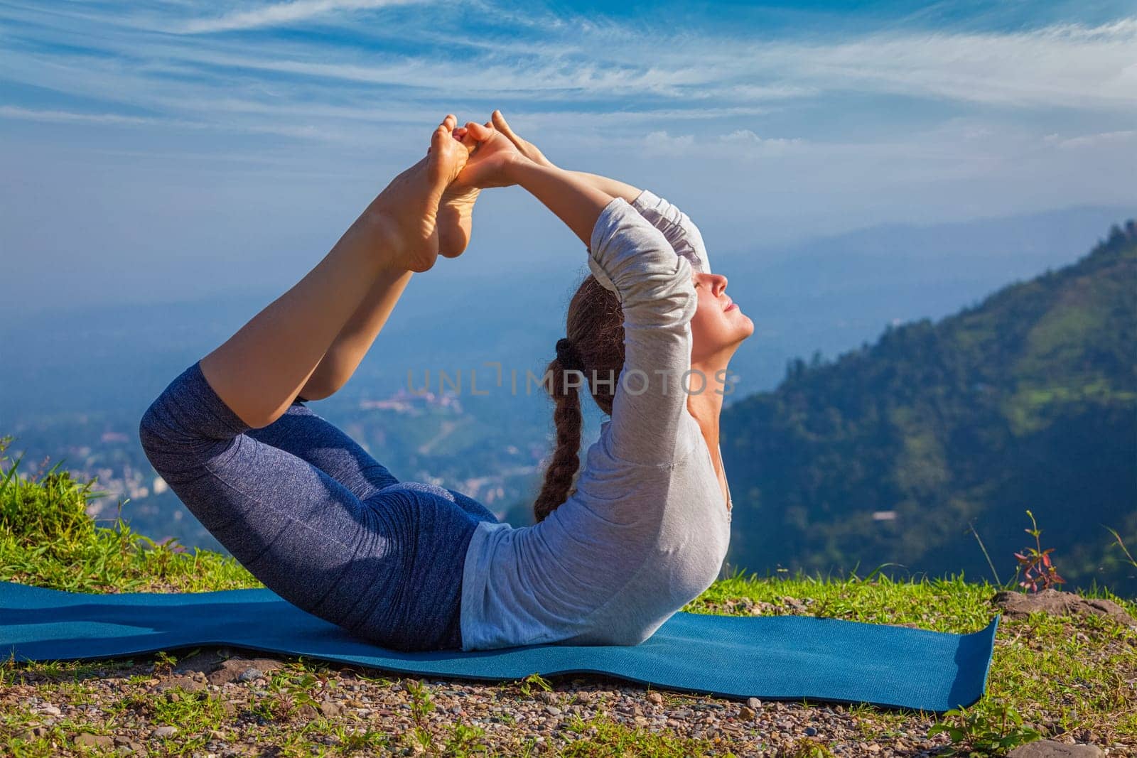 Yoga outdoors - young woman doing Ashtanga Vinyasa Yoga asana Dhanurasana - bow pose - in Himalayas mountains in the morning Himachal Pradesh, India