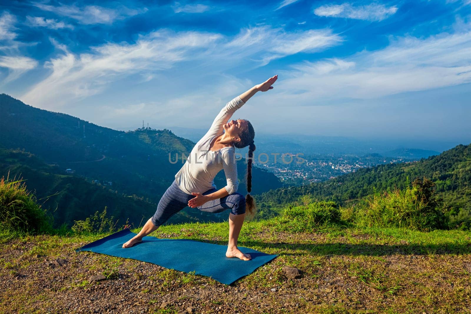 Woman practices yoga asana Utthita Parsvakonasana - extended side angle pose outdoors in mountains in the morning