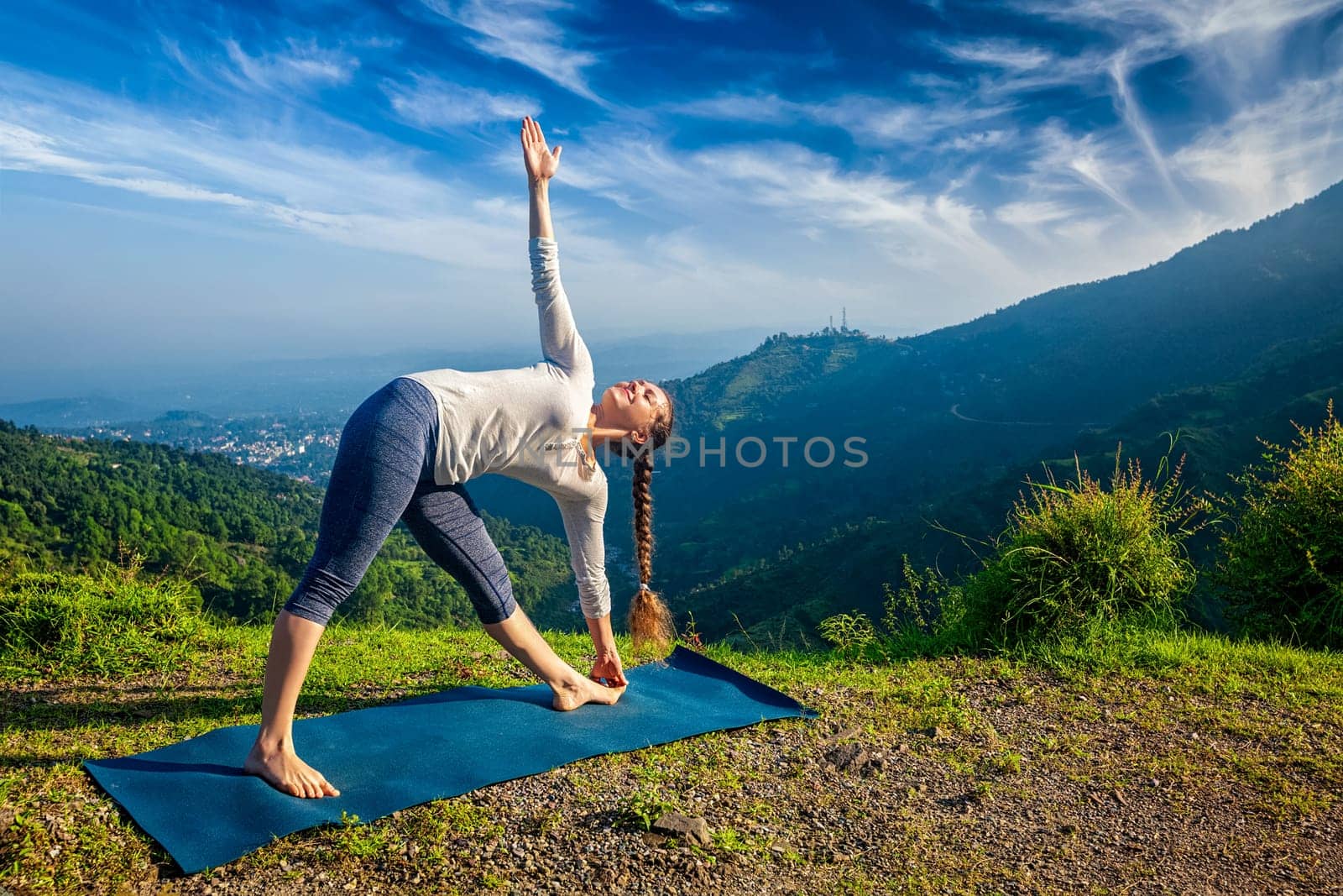 Woman doing Ashtanga Vinyasa yoga asana Utthita trikonasana - extended triangle pose outdoors in mountains in the morning