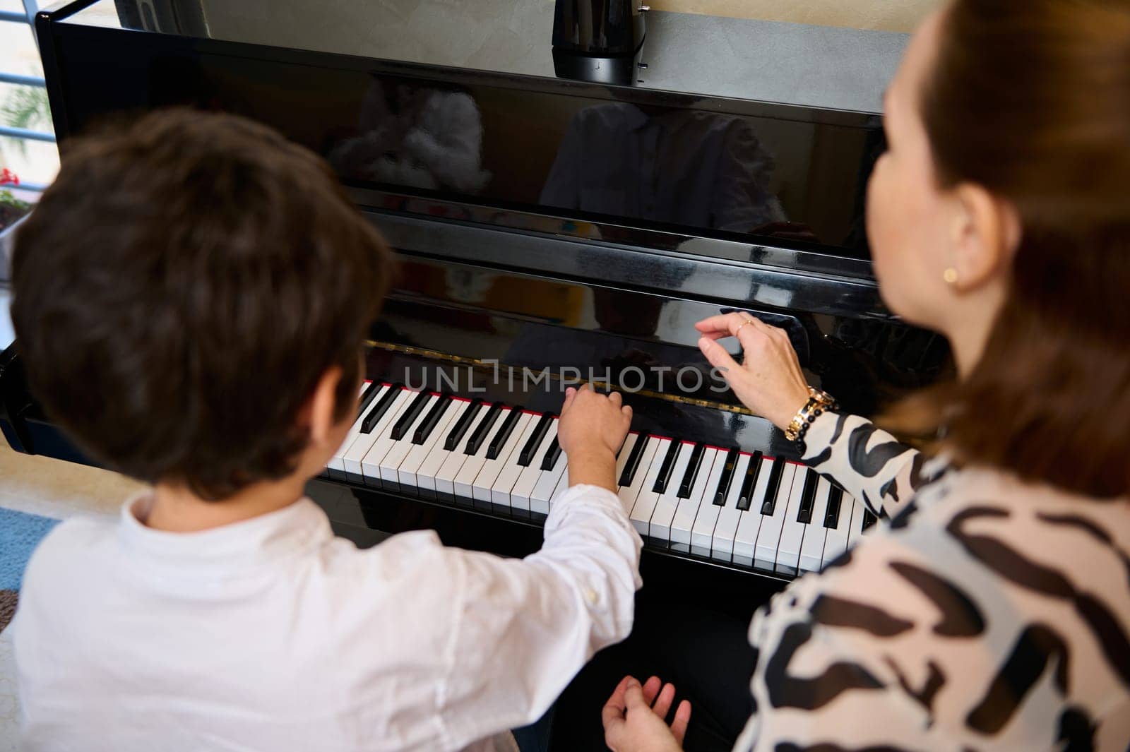 View from above of an adorable teen boy enjoying playing grand piano at home, creating music and song, performing soundtrack on the pianoforte, composing a melody during music lesson. by artgf