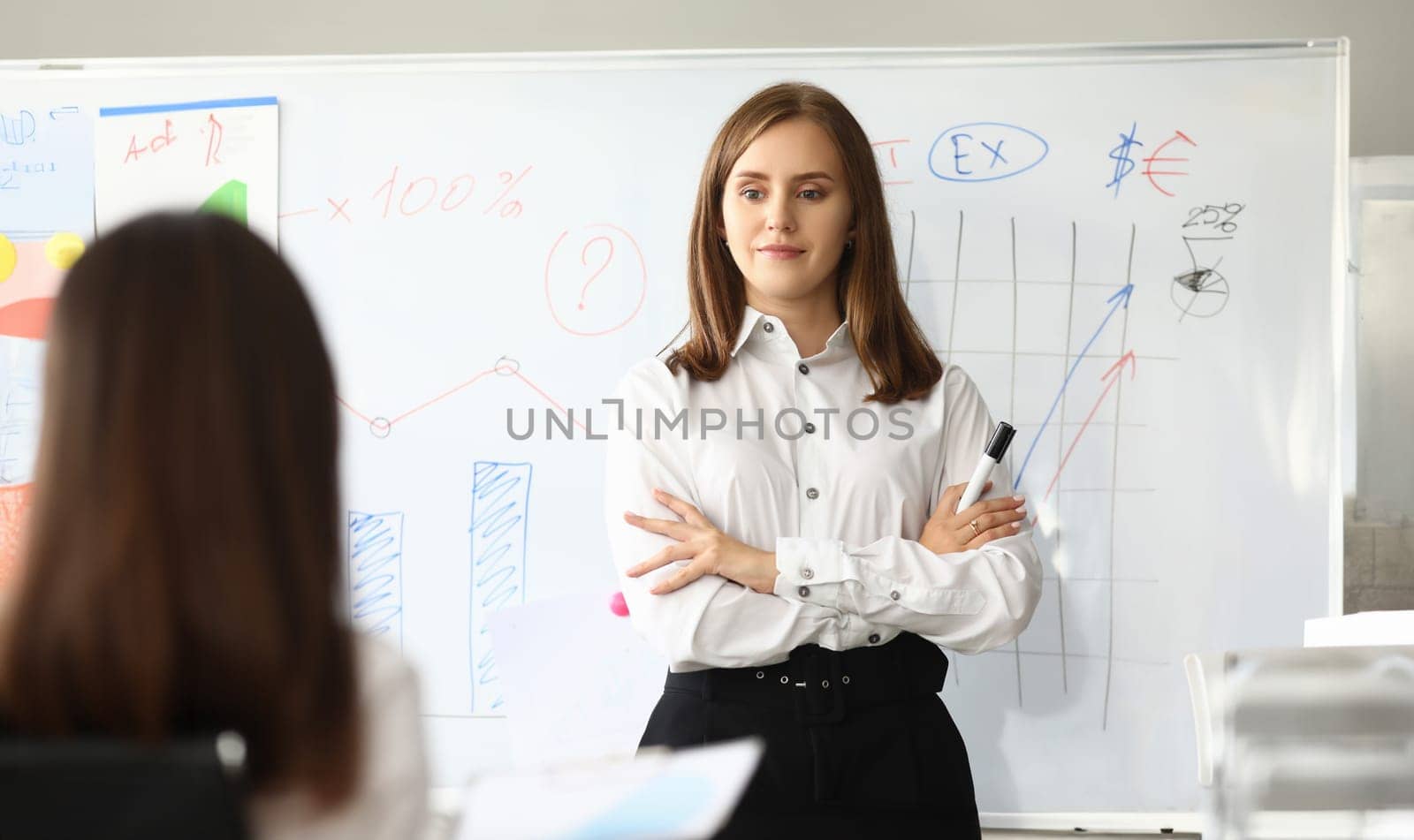 Portrait of Joyful female pointing at charts and graphs. Smart businesswoman standing at comfortable workplace and looking at somebody with calmness. Accounting office concept