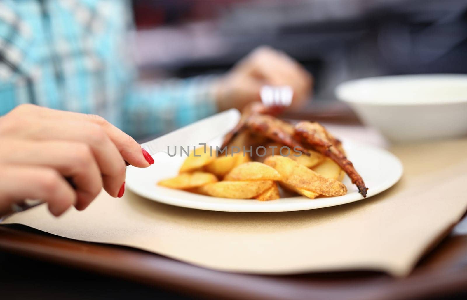 Woman hold knife and fork in her hand. White plate of potatoes and chicken on table.