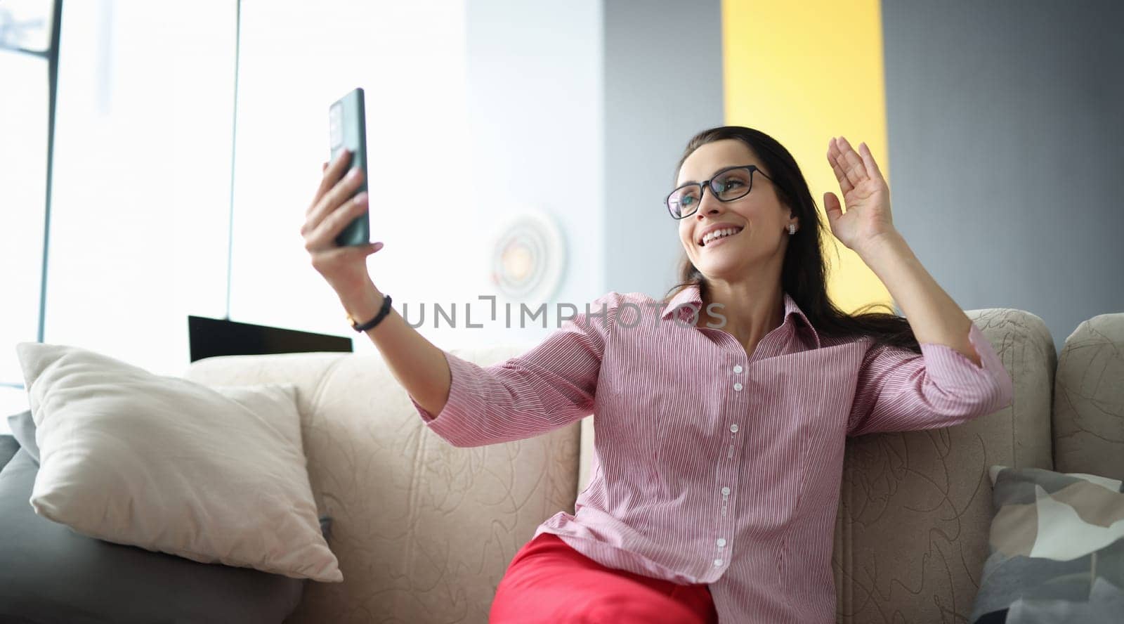 Beautiful woman in glasses wave hello on internet connection. Person talk online through phone at home.