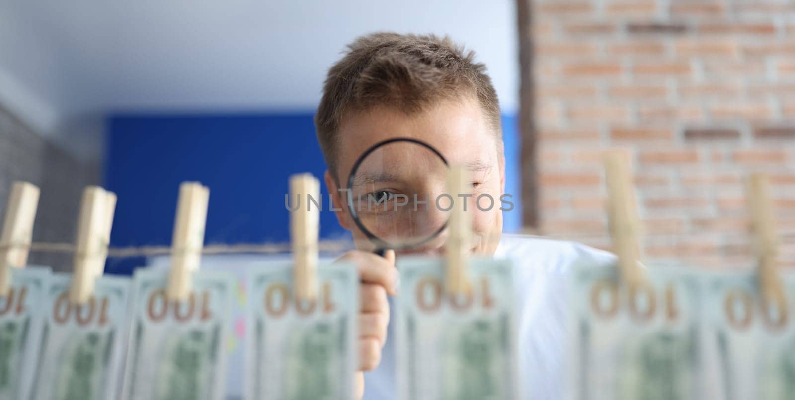 Man examines money through magnifying glass. Many hundred dollars hang on rope on clothespins.