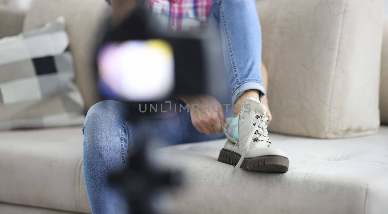 Woman puts on warm boot with her foot on sofa in front of camera close-up. Online earnings blogging concept.