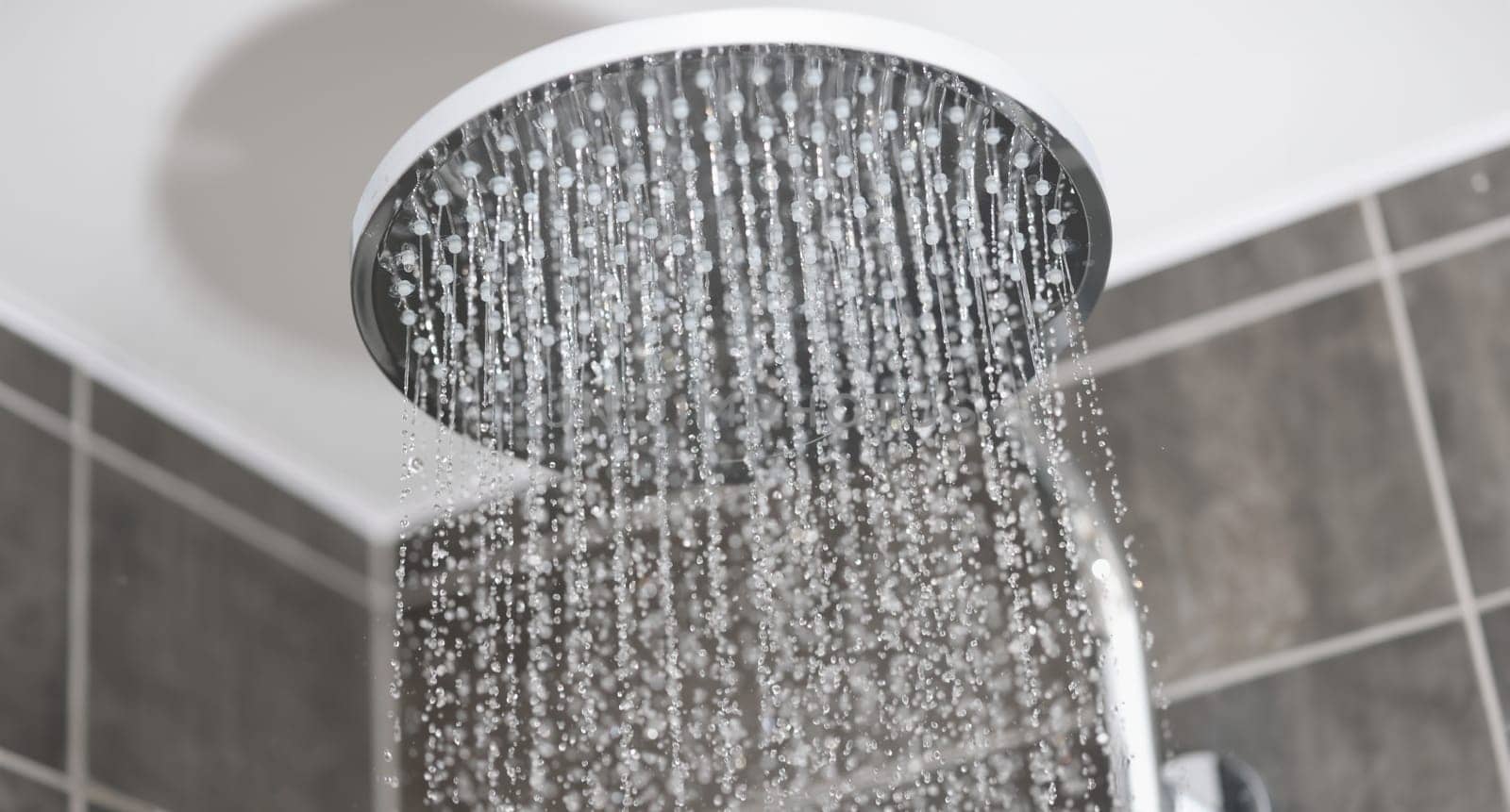 Close-up of water flows in small jets from metal rain shower in bathroom. Morning hygiene procedures concept.