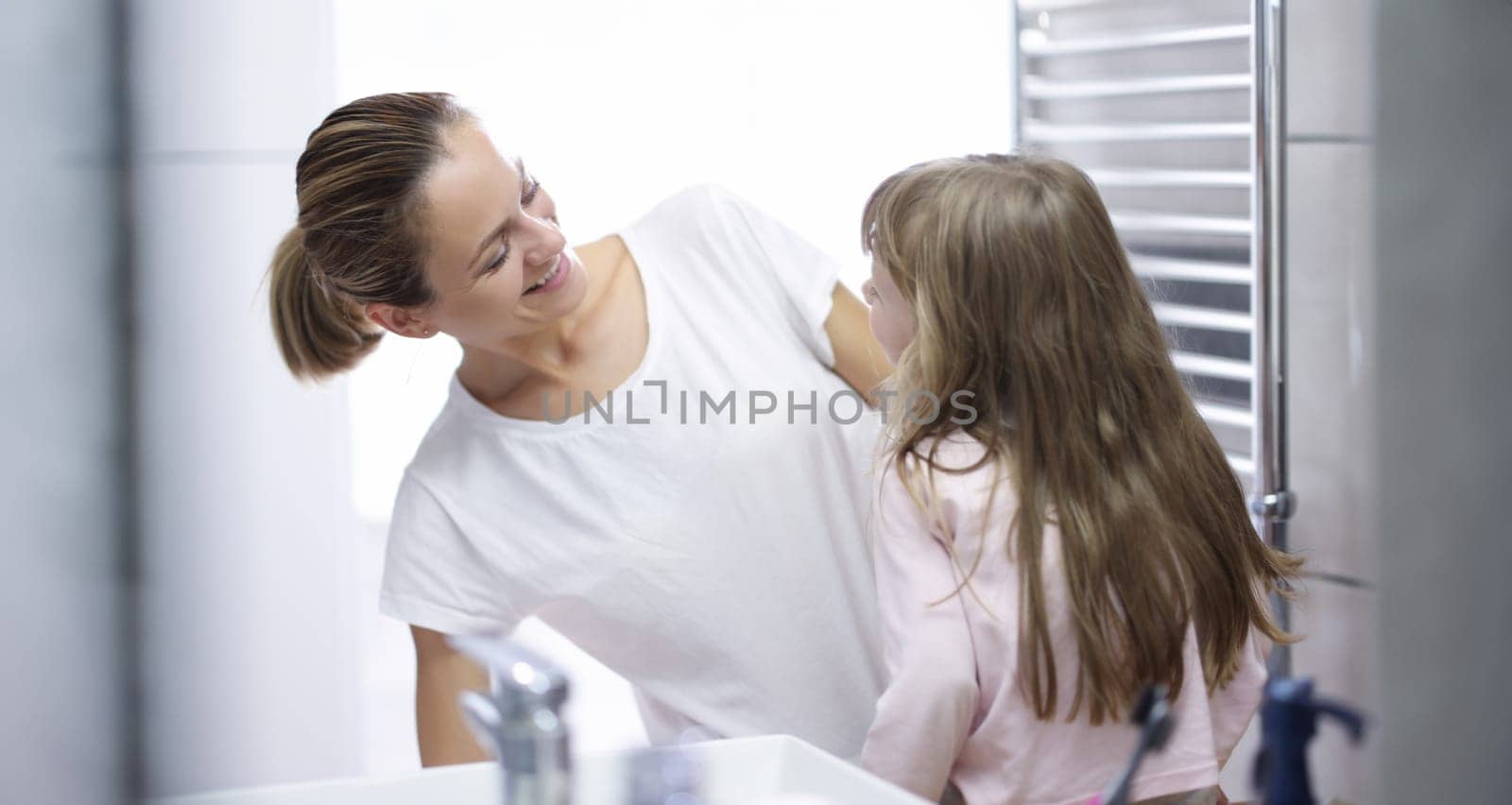 Young woman mother looking at baby and smiling in bathroom portrait. Daily morning hygiene procedures for children concept.