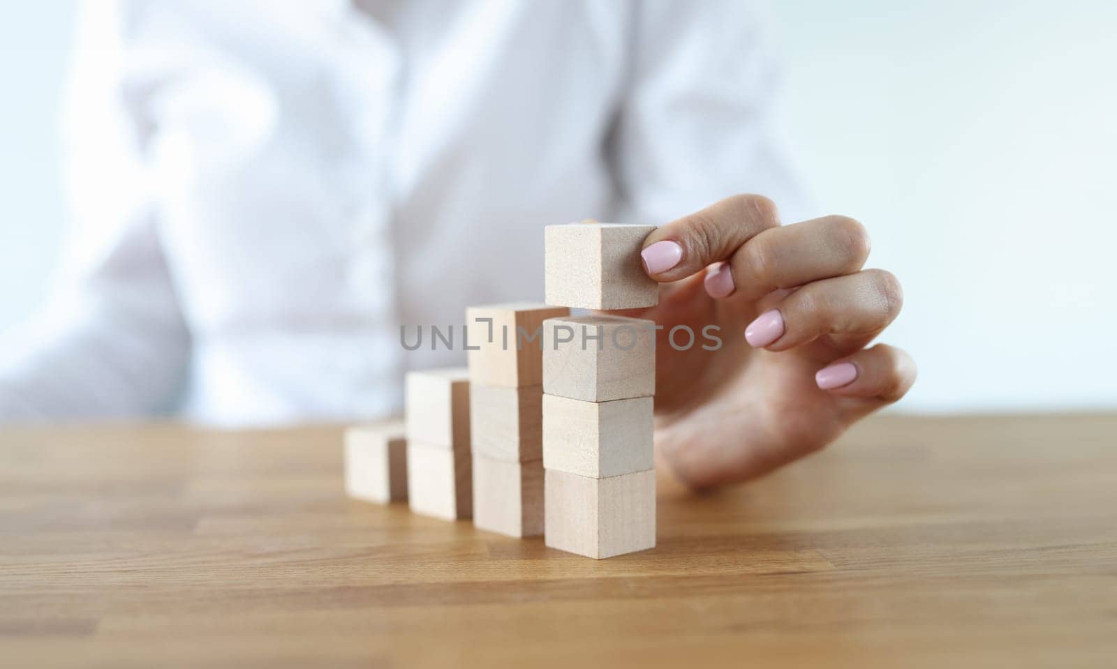 Woman build tower from wooden cubes on table close-up. Career growth up stairs. Female hand put cube one by one.