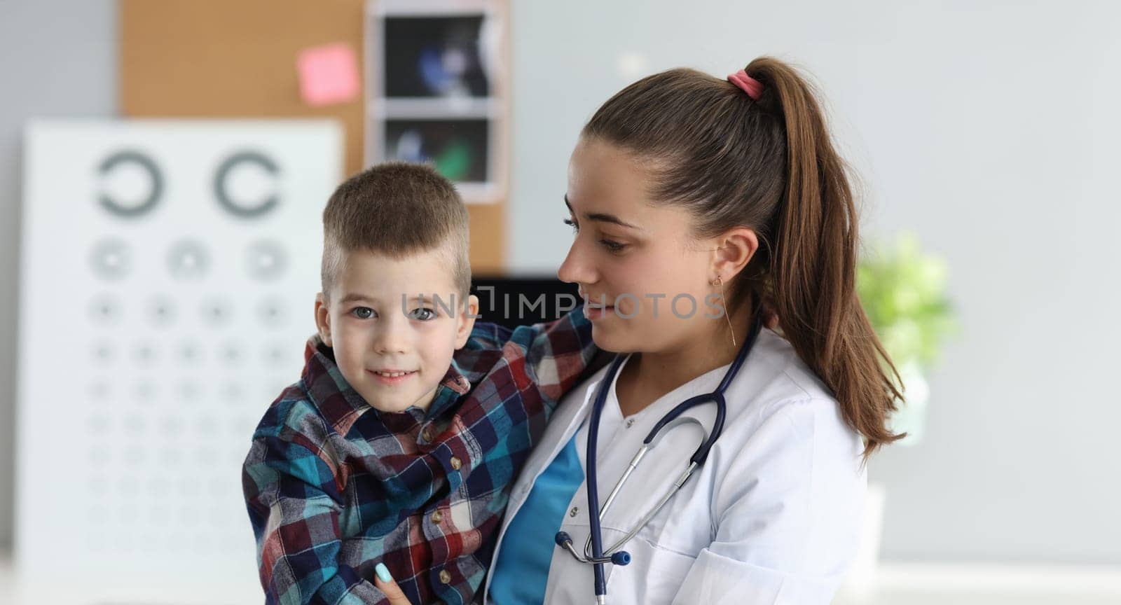 Close-up of female doctor carrying kid in arms. Professional pediatric with stethoscope on neck. Cheerful and friendly atmosphere. Planned checkup and modern medicine concept