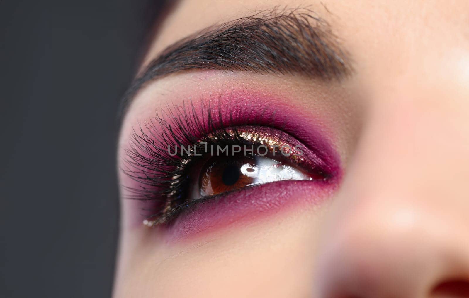 Close-up of female eye with bright trendy makeup. Professional maquillage in burgundy colors with golden glitters. Perfect long eyelashes. Beauty and decorative cosmetics concept