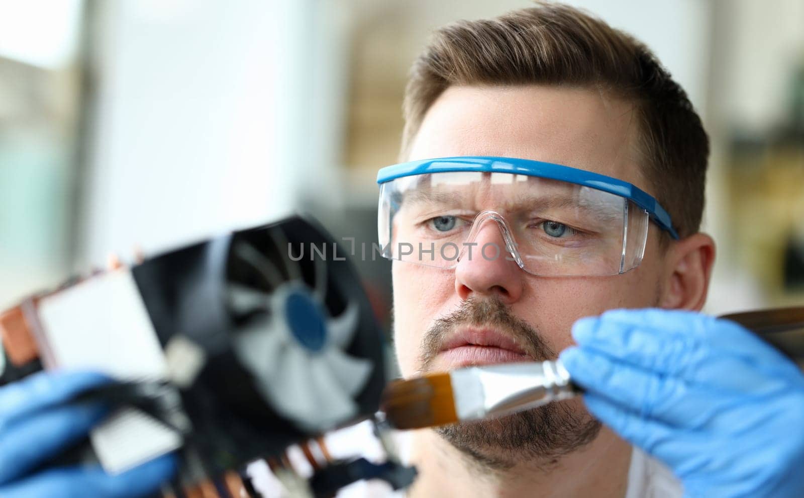 Close-up man goggles mends mechanical part device. Replacement thermal paste processor, lubrication active cooling system. Guy works at home during quarantine. Device repair in your apartment
