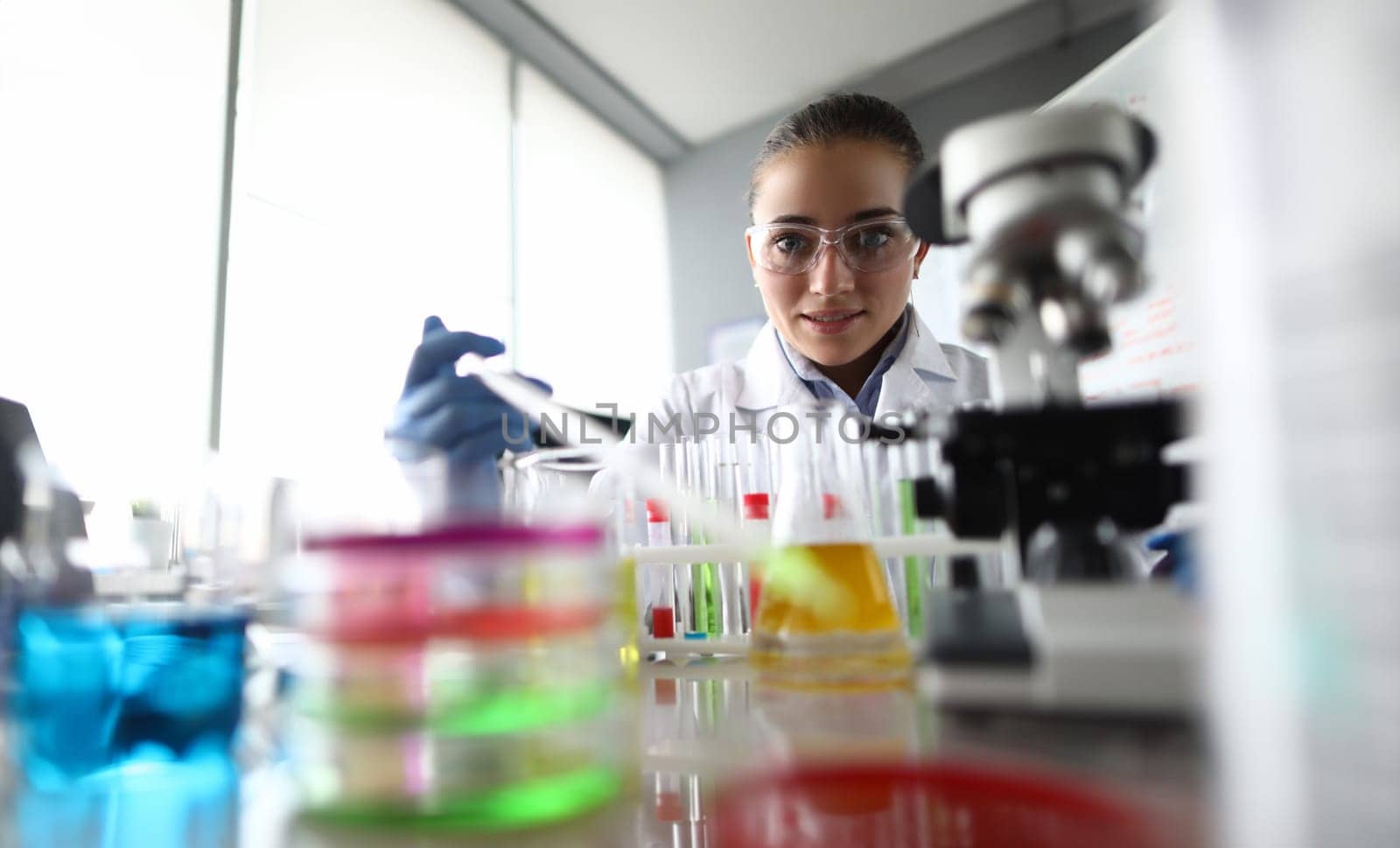 Portrait of smiling scientist adding reagent in fluid for experiment. Laboratory making chemical experiment in lab. Chemical experiments and investigations concept