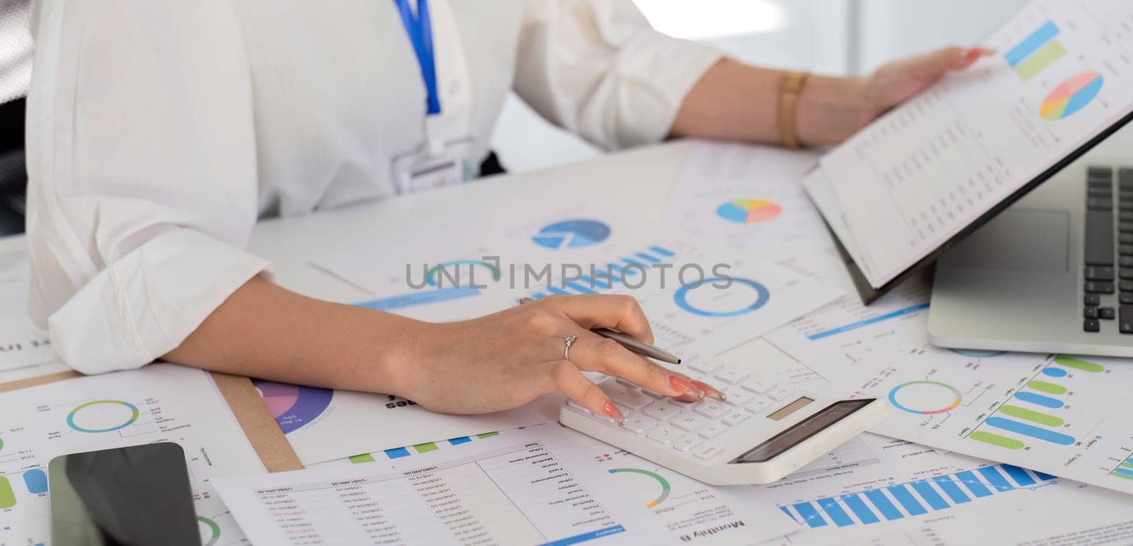 Close up, Beautiful Asian businesswoman uses a calculator to calculate numbers on company stock charts in a white office..