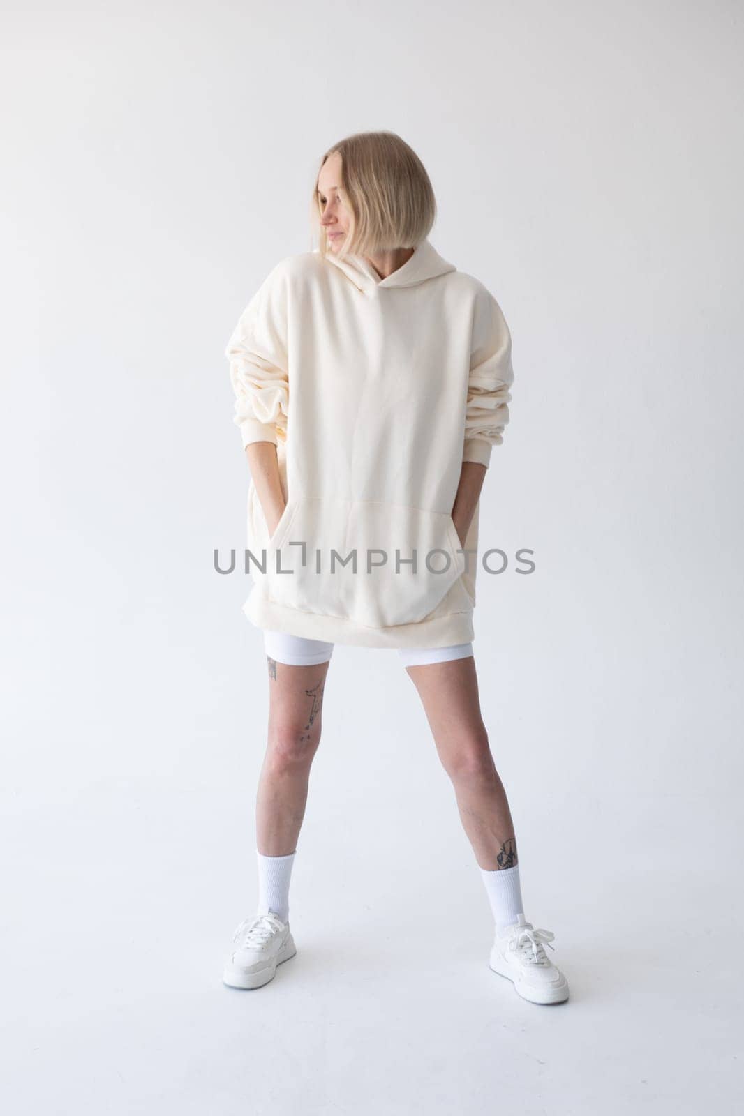 Beautiful blonde woman posing in white hoodie and leggings posing against white background by Freeman_Studio