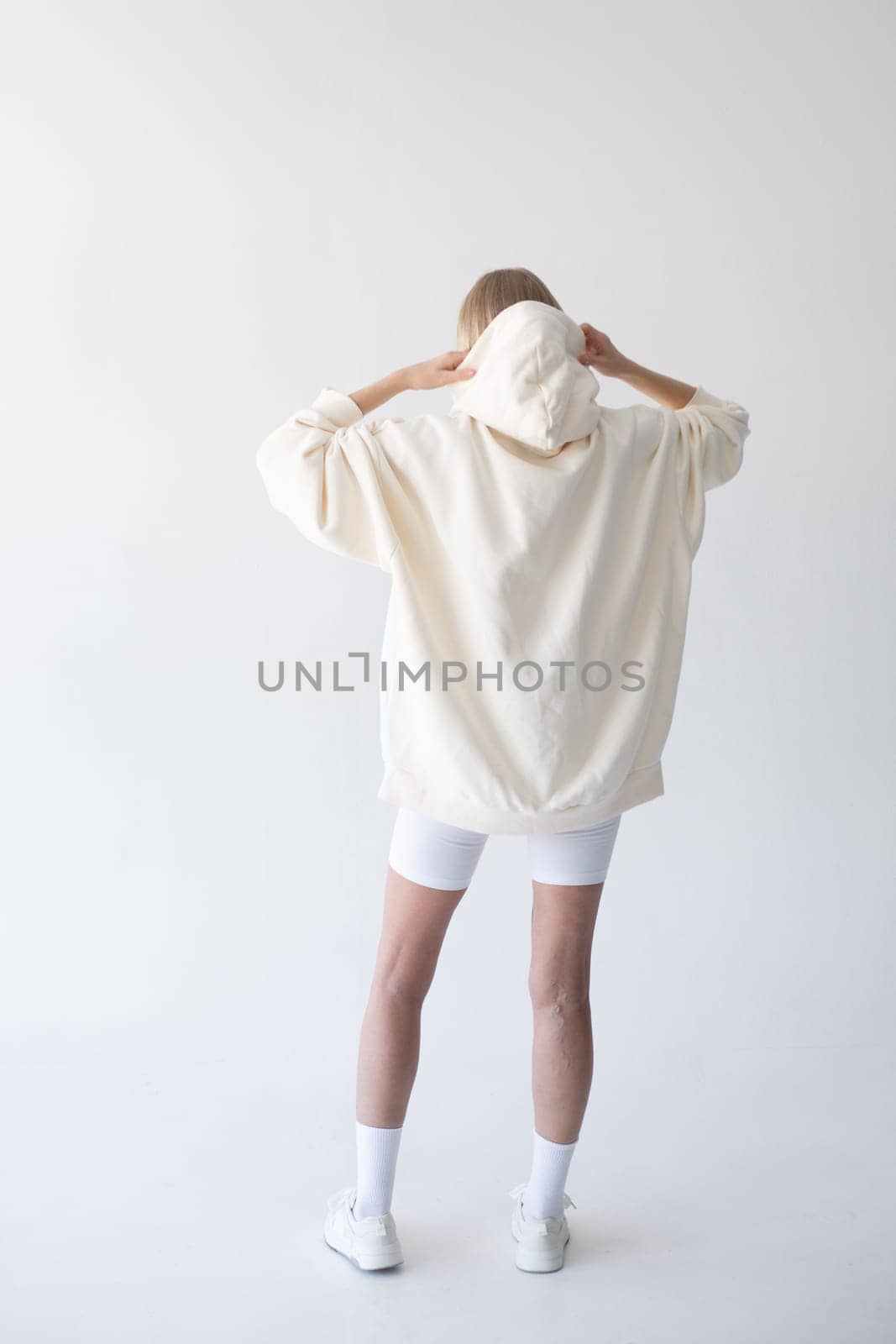 Beautiful blonde woman posing in white hoodie and leggings posing against white background. High quality photo