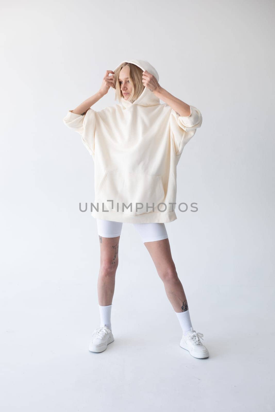 Beautiful blonde woman posing in white hoodie and leggings posing against white background. High quality photo