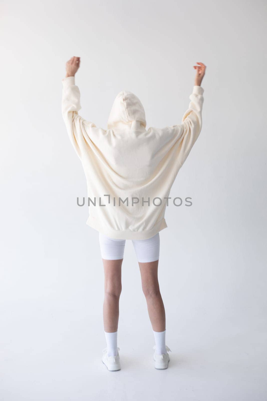 Beautiful blonde woman posing in white hoodie and leggings posing against white background. Posing with his back. by Freeman_Studio