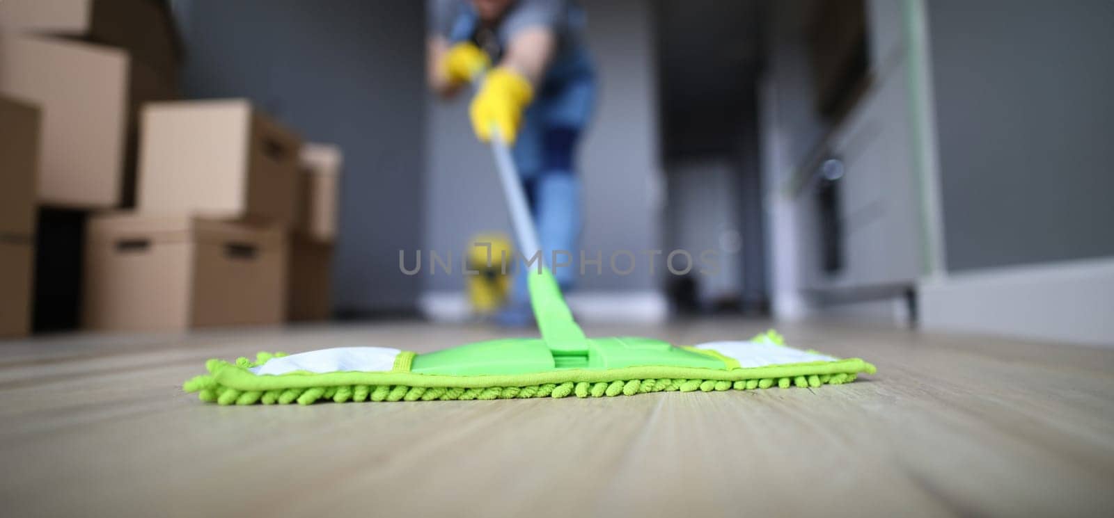 Male hand with yellow protective gloves hold green plastic mop close-up. Cleaning after repair concept