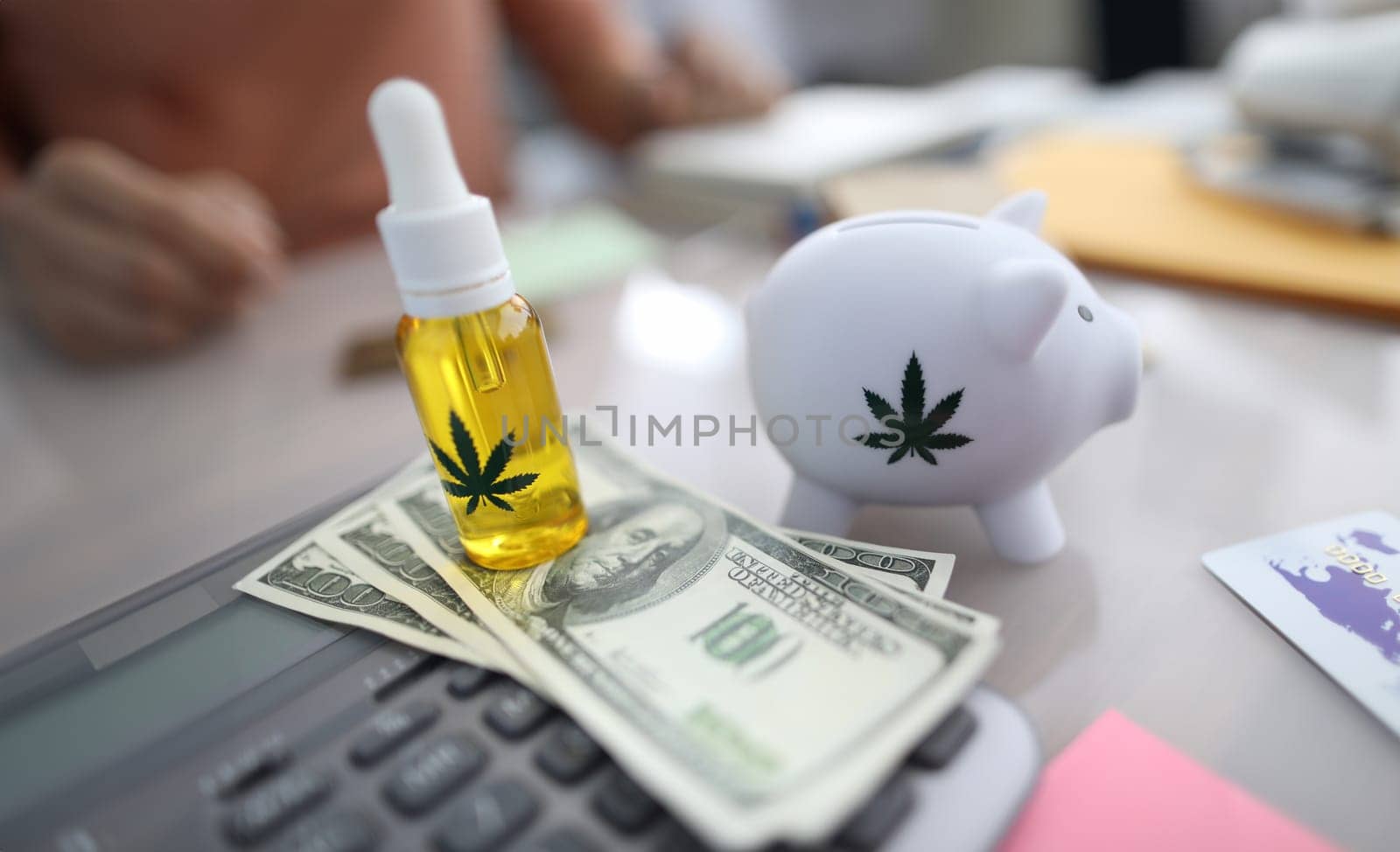 Close-up of white piggy bank with marijuana sign, cannabinoid oil in bottle with pipette. Cash on table. Person paying for pain medication. Painkillers concept