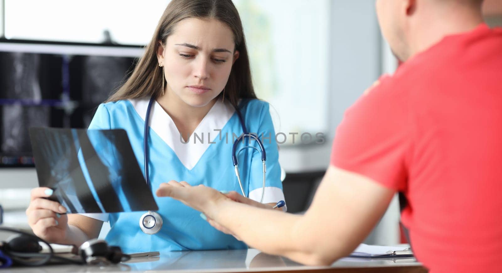 Close-up of qualified doctor examining patients hand on medical appointment in clinic. Concentrated young woman holding diagnostic result. Modern medicine and x ray concept