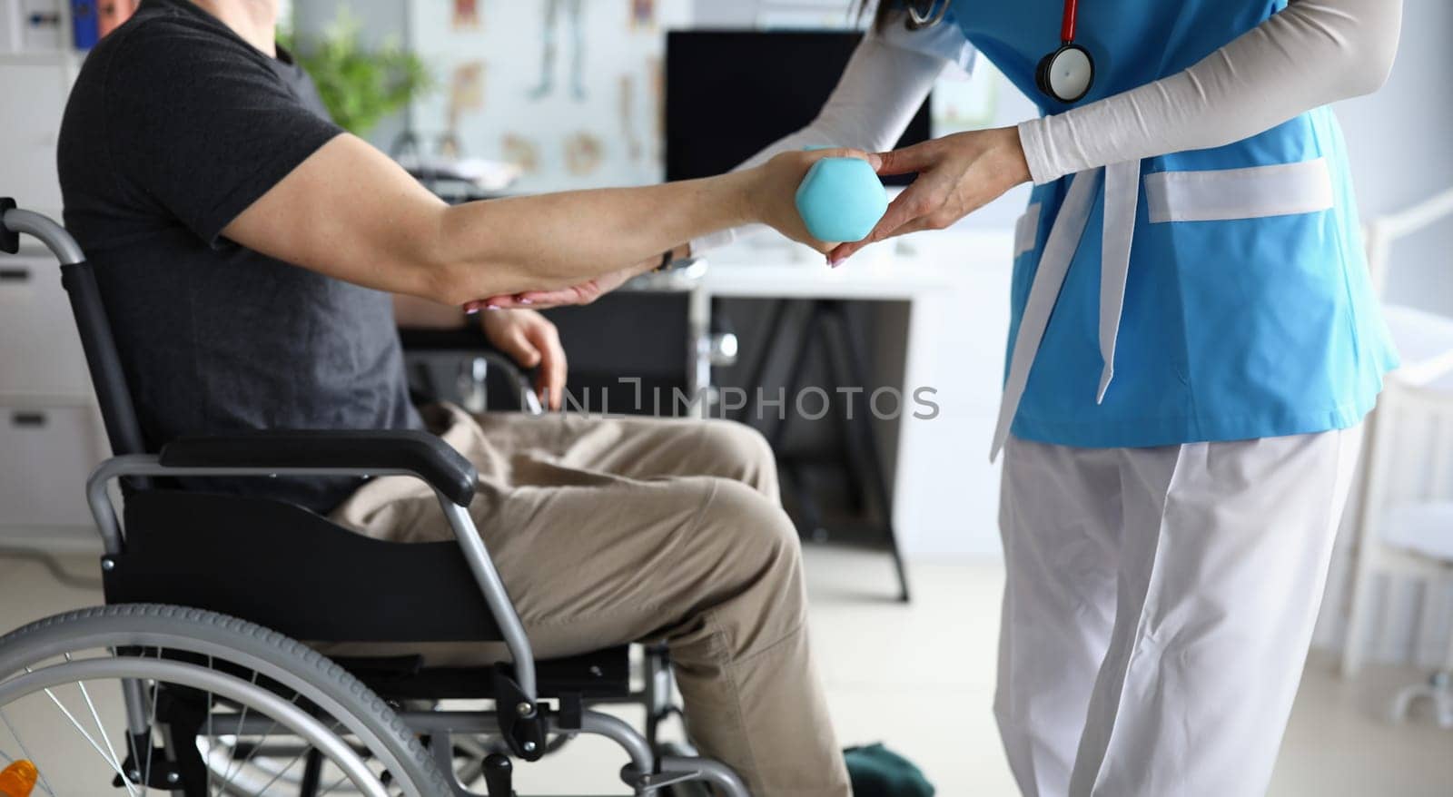 Female nurse helps lift dumbbell to disabled patient rehabilitation therapy by kuprevich