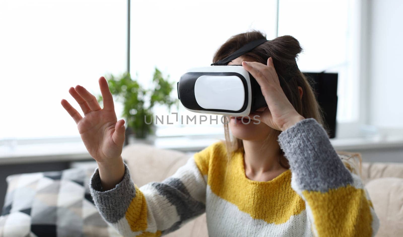 Girl sitting home looking through virtual glasses. Virtual reality simulates exposure and response to exposure, gaming. Young woman on sofa experiencing peace and positive emotions