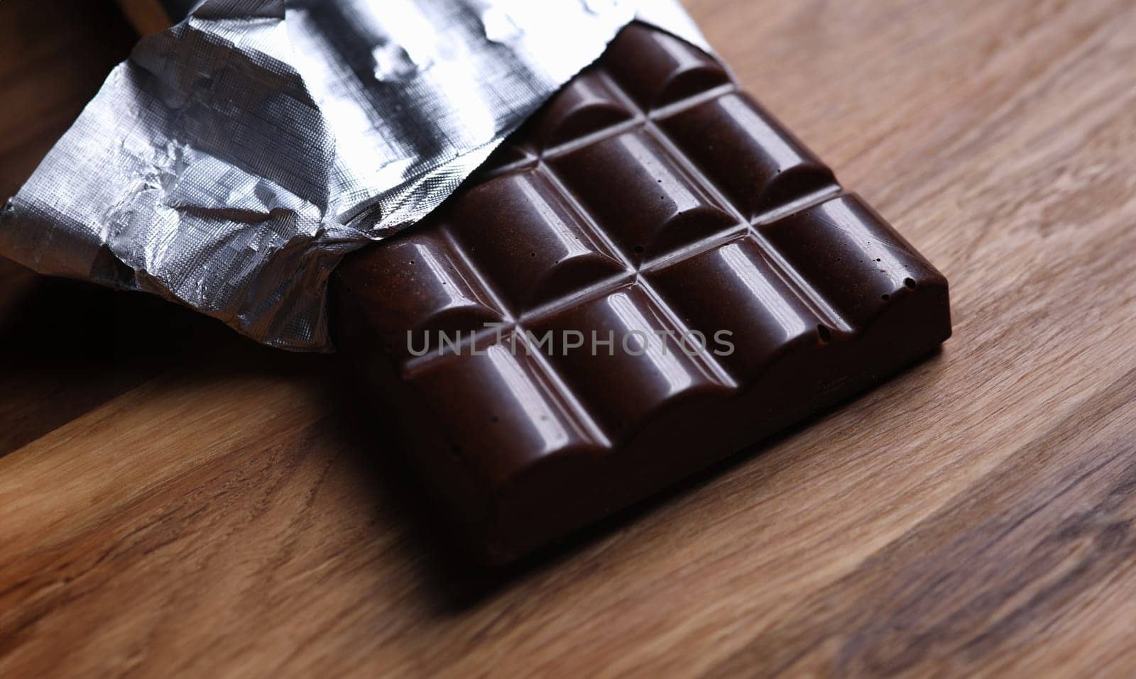 Close-up of dark chocolate bar in foil with open cover laying on wooden table. Unpacked sweets with nut. Calories and antioxidant. Sweet and yummy dessert concept