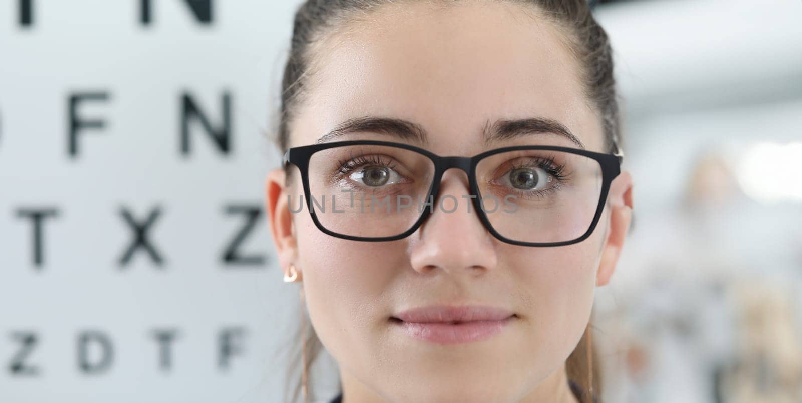 Close-up of smiling eye doctor wearing vision glasses and posing on board with letters. Checkup eyesight. Copy space in left side. Modern medicine and ophthalmologist concept