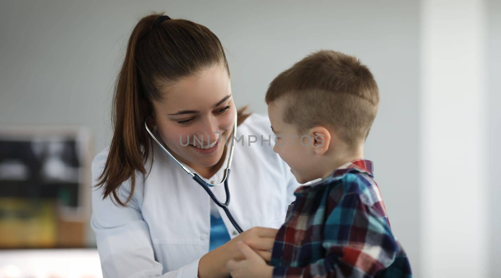 Close-up of smiling doctor examine child lugs. Lovely female doctor in medical gown wearing stethoscope. Modern medicine and pediatric appointment concept