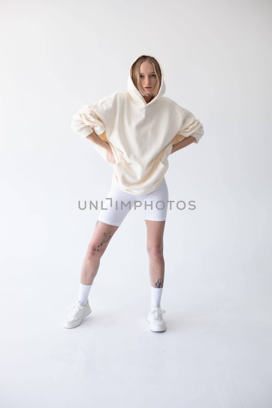 Beautiful blonde woman posing in white hoodie and leggings posing against white background by Freeman_Studio