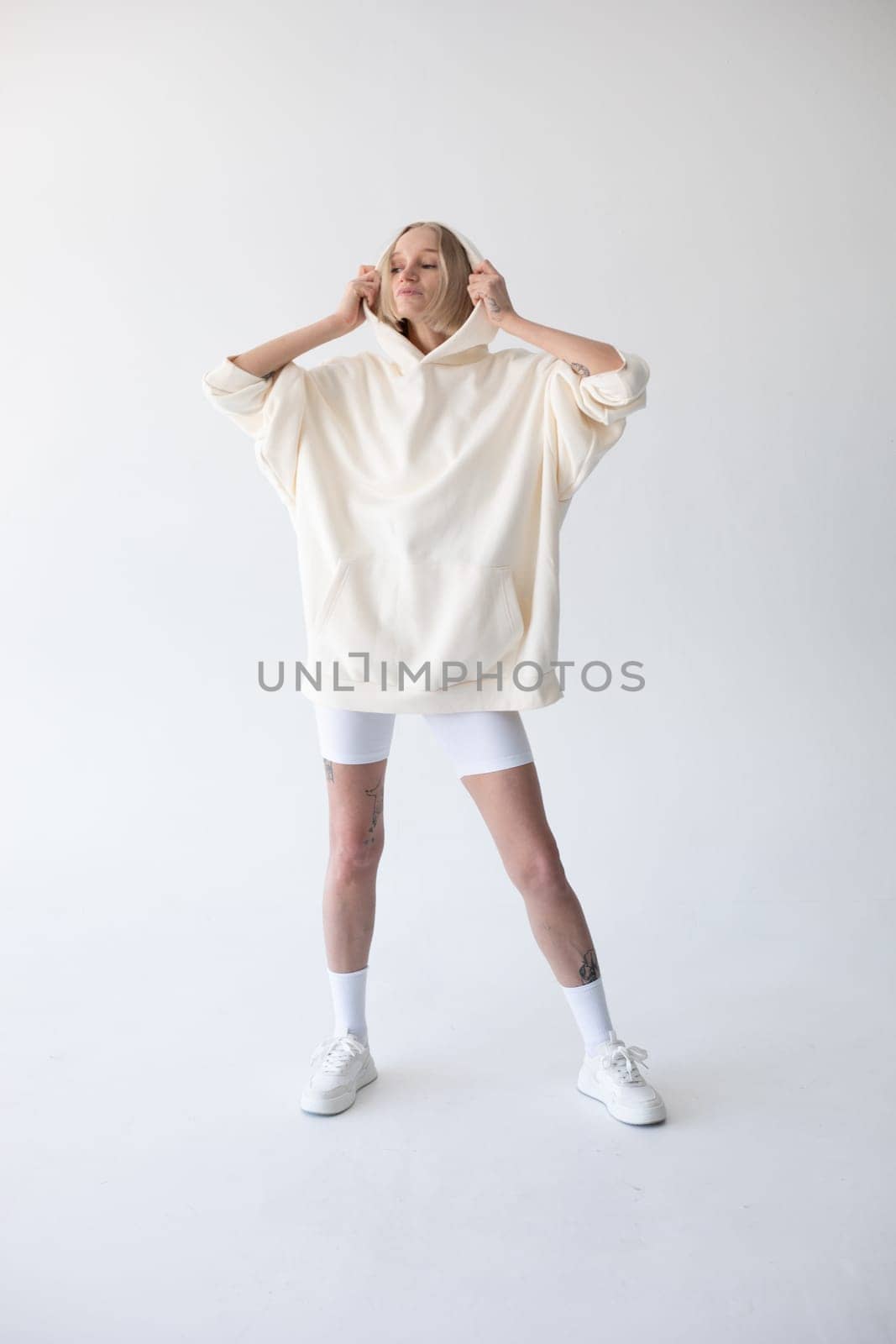 Beautiful blonde woman posing in white hoodie and leggings posing against white background by Freeman_Studio