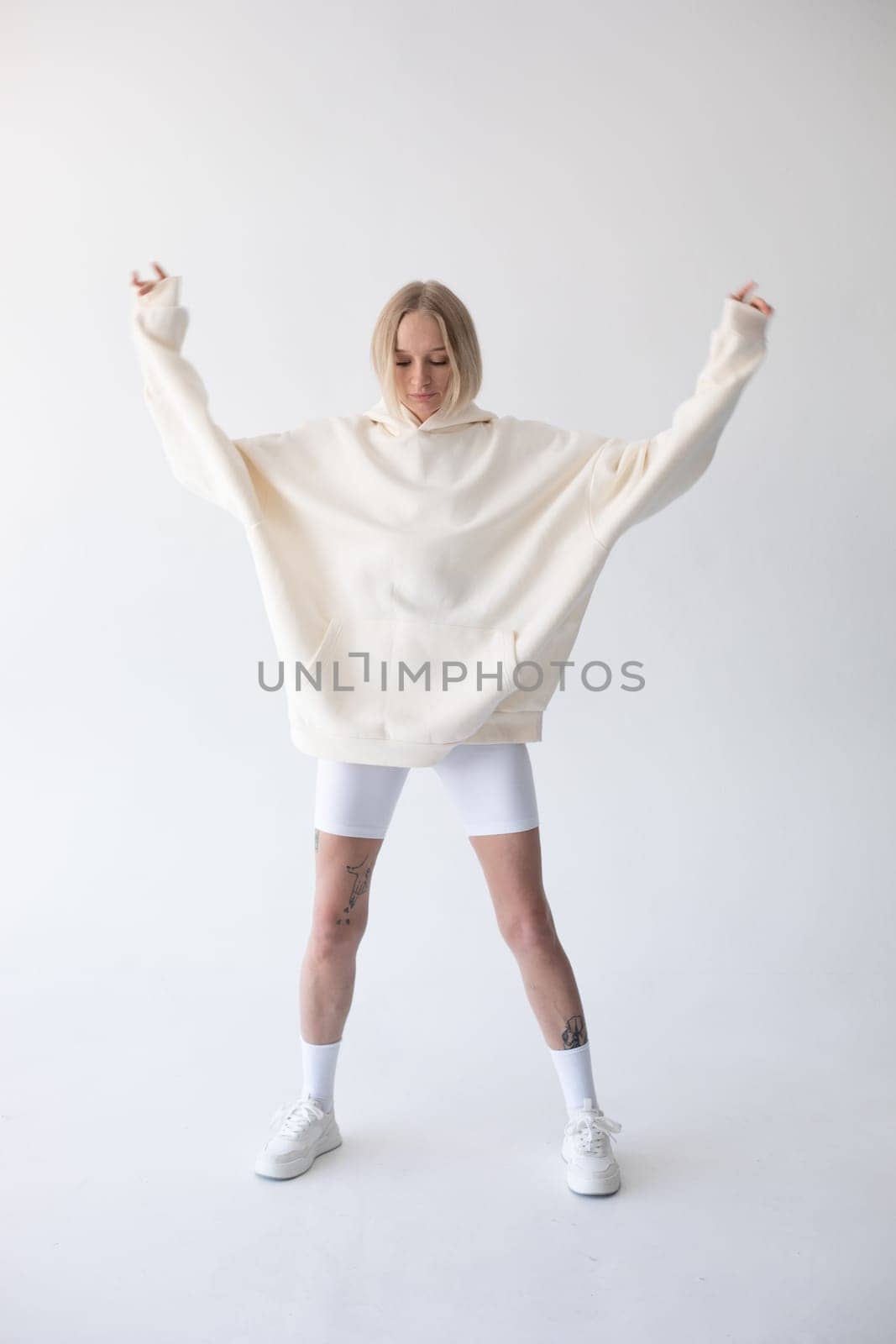 Beautiful blonde woman posing in white hoodie and leggings posing against white background. High quality photo