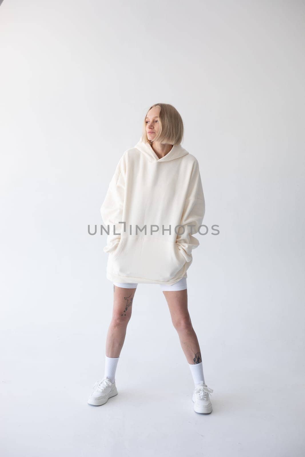 Beautiful blonde woman posing in white hoodie and leggings posing against white background. High quality photo