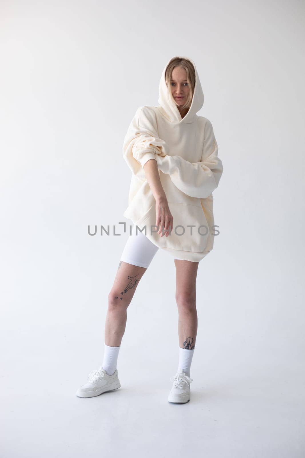 Beautiful blonde woman posing in white hoodie and leggings posing against white background by Freeman_Studio