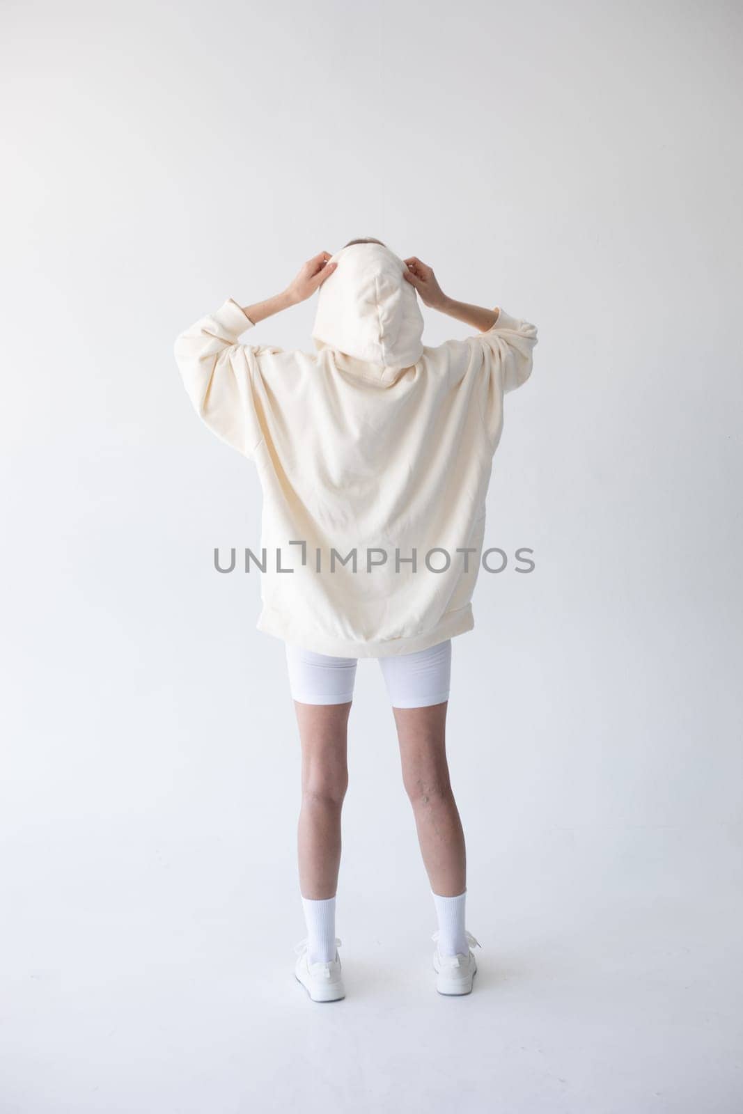 Beautiful blonde woman posing in white hoodie and leggings posing against white background. Posing with his back. by Freeman_Studio