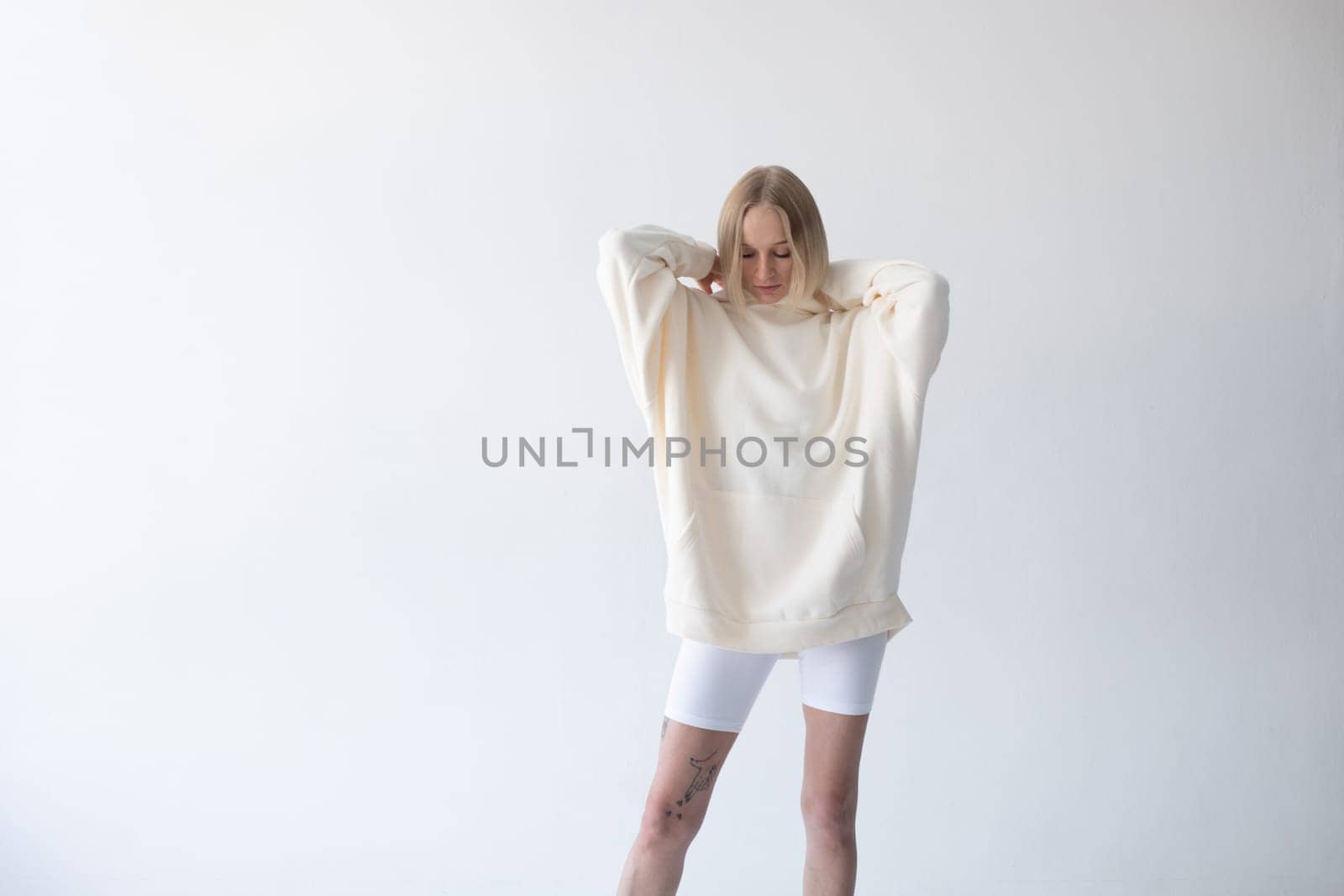 Beautiful blonde woman posing in white hoodie and leggings posing against white background. High quality photo